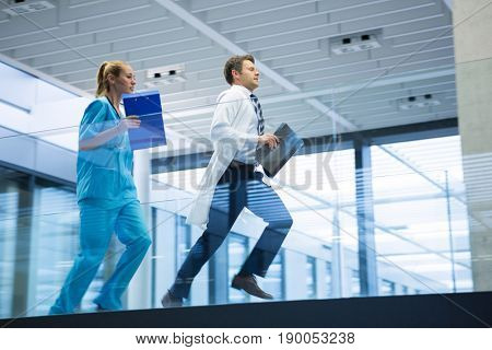 Male doctor and nurse running with x-ray report in corridor at hospital