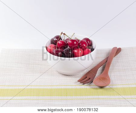 Cherries in white bowl and wooden spoon on white background