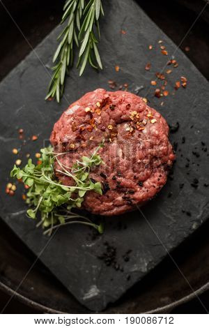 Raw ground beef meat steak cutlets with herbs and spices on black board. Restaurant