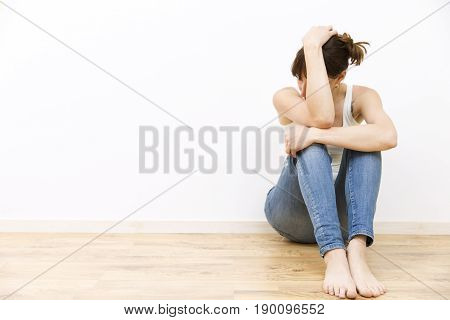 Depressed sad young woman sitting on floor holding her head