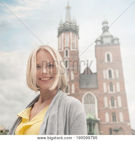 Female tourist in a yellow dress stands on a background of the church of St. Mary in Krakow. Basilica Mariacka. Krakow. Poland.