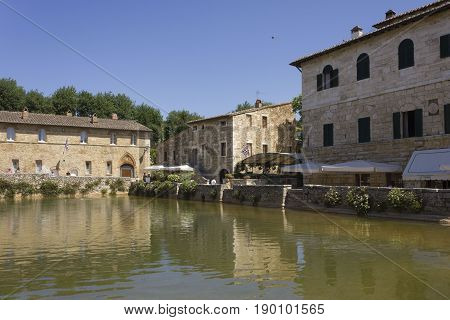 BAGNO VIGNONI, ITALY - JUNE 3 2017: Piazza delle sorgenti medieval square in Bagno Vignoni with a lake of hot spring water and people looking at it