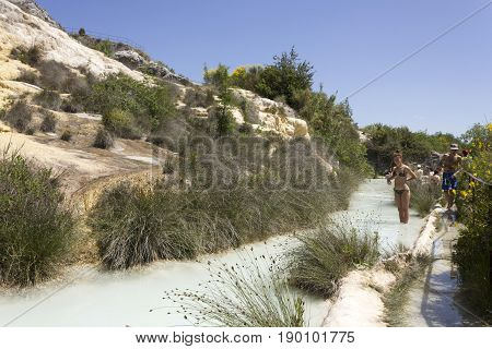 BAGNO VIGNONI, ITALY - JUNE 3 2017: People bathing in the free area of Bagno Vignoni in Tuscany Italy free accessible hot springs puddle trough vegetation