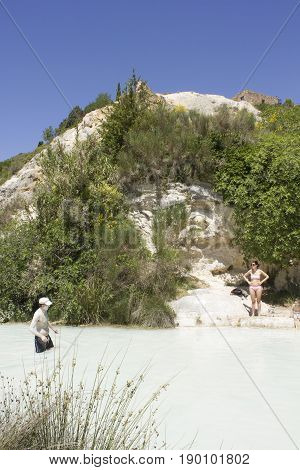 BAGNO VIGNONI, ITALY - JUNE 3 2017: People bathing in the free area of Bagno Vignoni in Tuscany Italy free accessible hot springs puddle trough vegetation