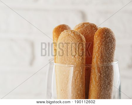 Close up view of ladyfinger biscuit cookie in glass jar on white brick wall background. Italian cookie savoiardi. Copy space.
