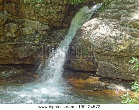 A waterfall cascading over a natural rock wall and merging with a deep pool at the Blue Hole in East Tennessee.