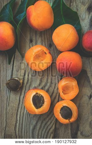 Fresh ripe colorful apricots halved and whole on weathered plank wood background kernel green leaves top view light matte filter