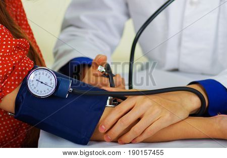 Close up of a young doctor using the stethoscope to hear the pulse while a woman is with a tensiometer in her arm, in a doctor consulting room background.