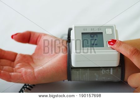 Close up of a young patient using an automatic tensiometer in her arm, in a doctor consulting room background.
