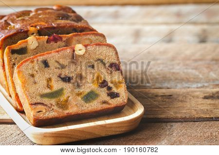 Homemade fruit cake on wood plate. Rum fruit cake with dried fruits made for Christmas celebration. Traditional homemade fruit cake for Christmas so delicious rich and moist on rustic wood table. Slice of delicious Christmas fruit cake.