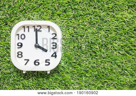 Closeup white clock for decorate in 4 o'clock on green artificial grass floor textured background with copy space