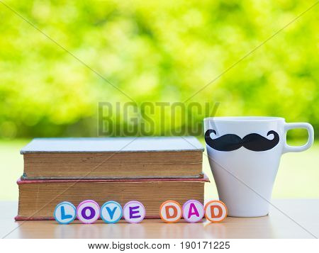 Father's day concept. LOVE DAD alphabet on stack of books gifts tea cup with black Mustache and flower on background