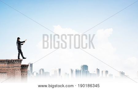 Businessman with blindfolder on eyes walking on building top