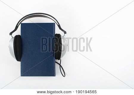 Audiobook on white background. Headphones put over blue hardback book, empty cover, copy space for ad text. Distance education, e-learning concept