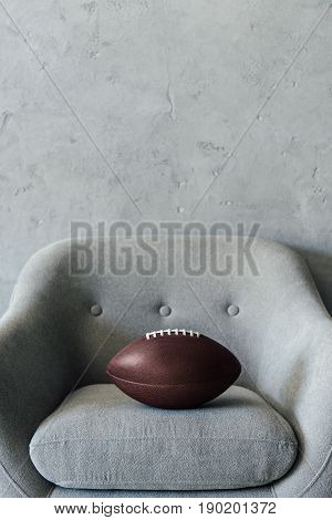 American Football Ball On Grey Textile Armchair At Empty Room