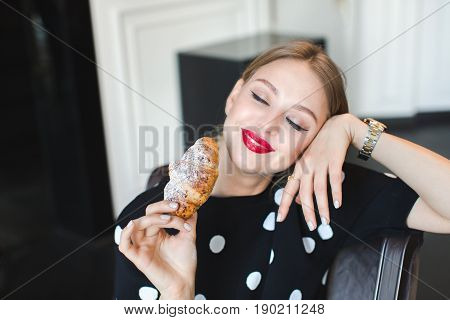 Close-up portrait of a beautiful young sweet girl eating a sweet croissant, bright makeup, skin, red lips, sexy