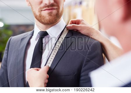 Closeup image of tailor taking measurements of jacket to fit bespoke business suit