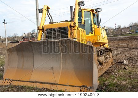 Bulldozer huge orange powerful construction machine with hydraulic piston of scoop and black wheels heavy industry bottom view blue sky on background