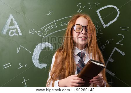 Girl schoolgirl knowledge, girl at the table wearing glasses at the blackboard.