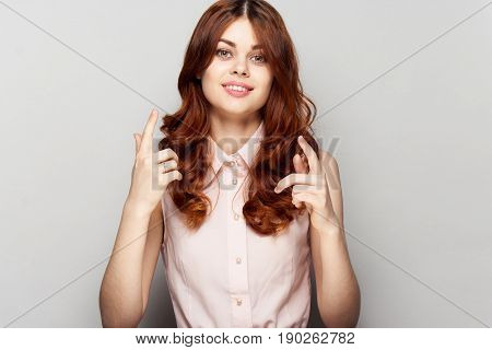 Woman in pink dress on a gray background shows a finger.