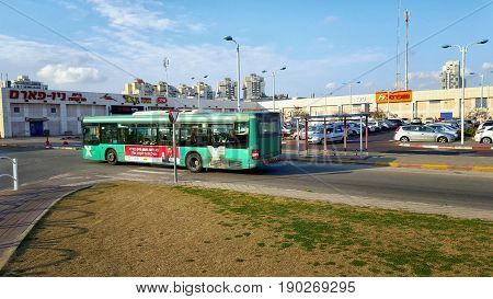 Rishon LeZion, Israel-February 10, 2016: Green bus of Egged company goes along central bus station in Rishon LeZion. Some commercial signs are seen on the two story building, There are big parking lot for private cars in front of it. It is located Hahista
