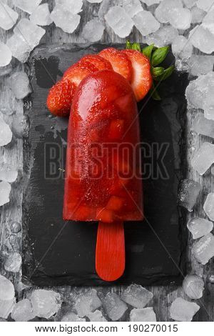 high-angle shot of a homemade ice pop made with natural strawberries, on a natural slate tray surrounded by ice