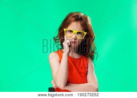 Funny little girl in bright glasses on a colored background posing.