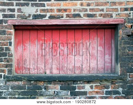 baorded up long window in an old victorian building with faded wood and peeling red paint