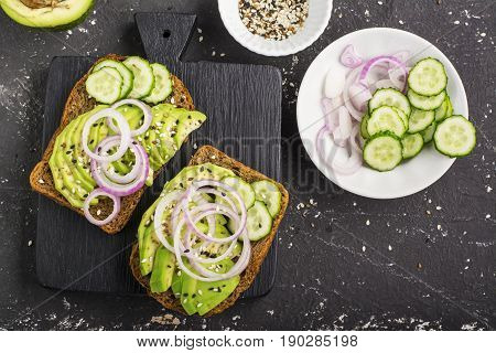 Sandwiches on toast grain dark bread with slices of avocado, sweet pink onions and multi-colored sesame seeds. Top view.