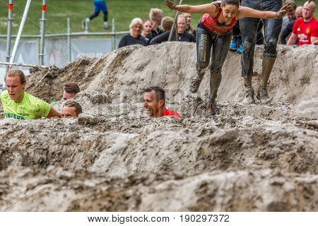 Stockholm Sweden - June 03 2017: Front view group of caucasian men an women in a mud obstacle struggling to complete the course of the annual event Toughest Stockholm.