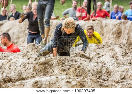 Stockholm Sweden - June 03 2017: Close up front view one caucasian woman struggling in a mud obstacle to complete the course of the annual event Toughest Stockholm. People in the background.