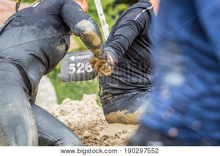 Stockholm Sweden - June 03 2017: Close up view two caucasian woman struggling in a mud obstacle holding hands to complete the course of the annual event Toughest Stockholm.