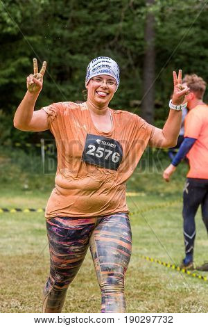 Stockholm Sweden - June 03 2017: Close up front view one caucasian chubby woman running. Wet happy and smiling after completing a mud obstacle at the annual event Toughest Stockholm. One person in the background.