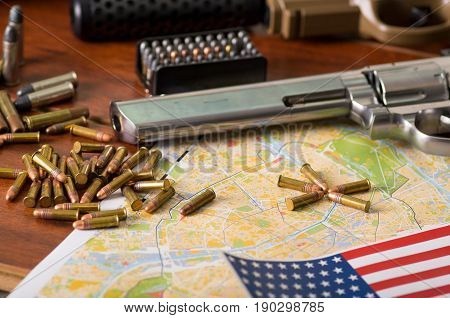 Close up of a shotgun and a revolver, cartridge belt with bullets with a blurred United States flag on a map, on wooden table.