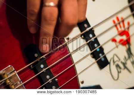 Bass Guitar In Playing Musician Hands Close-up. Focus On Bass Guitar Neck In Player Hands. Unrecogin
