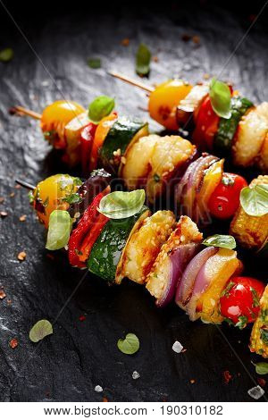 Grilled vegetarian skewers with halloumi cheese and mixed vegetables on black background, closeup