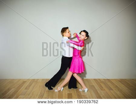 The young boy and girl posing at dance studio on gray. The ballroom dancing concept