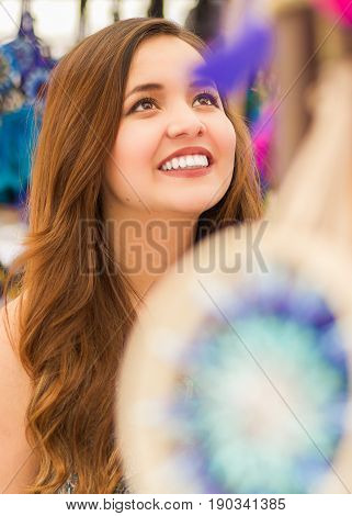 Close up of a beautiful smiling young woman looking a colorful andean traditional catchdreamers, in colorful market fabrics background.