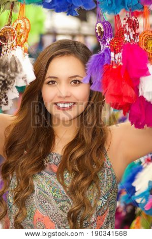 Beautiful smiling young woman hiding behind a colorful catchdreamer, in colorful market fabrics background.