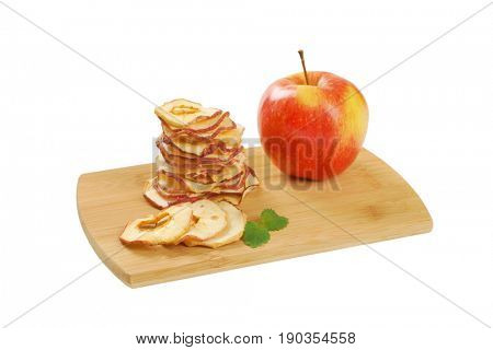 stack of dried apple chips and fresh apple on wooden cutting board