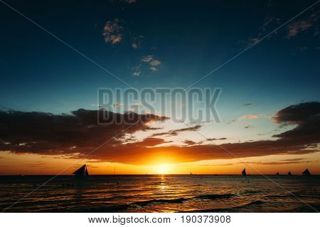 Dramatic orange and blue sea sunset with sailboats in tropical country . Wide angle. silhouettes of boats the solar disk. Philippines Boracay