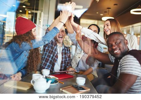 Multi-ethnic team of talented designers congratulating each other with successful completion of joint project and giving high five