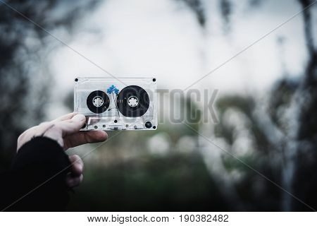 A man holds in his hand an old cassette tape with a flower inside against the sky and trees. Concept: nostalgic time.