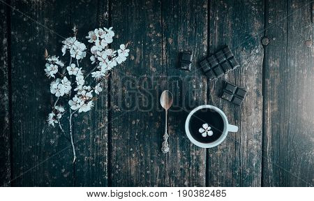 Mug of coffee with chocolate and flowering branches of peach on old wooden.