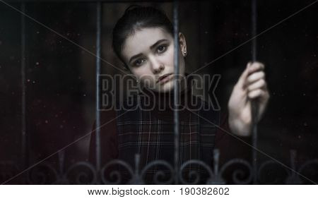 The girl with a sad look left behind the iron gates of the castle. dark scarlet color.