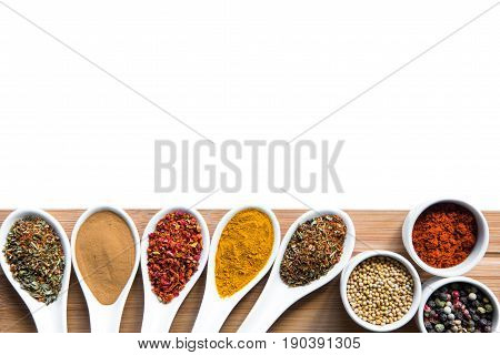 Various Spices And Herbs In Spoons Snd Bowles On Wooden Tabletop Isolated On White