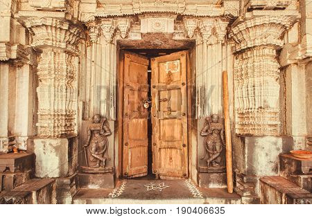 Indian traditional style design at entrance of historical Hindu temple with collumns wooden door and sculptures, India