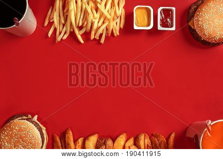Burger and Chips. Hamburger and french fries in red paper box. Fast food on red background. Hamburger with tomato sauce. Top view, flat lay with copyspace