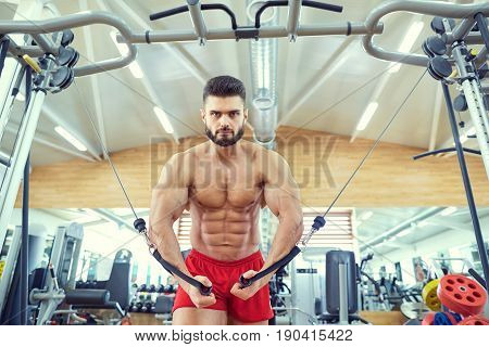Bodybuilder does exercises on  simulator in the gym.