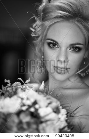 The face of a beautiful bride with a bright make-up expressive blue eyes long black eyelashes with a voluminous hairdo with fresh flowers. With a smile on her face she holds a bouquet black and white frame